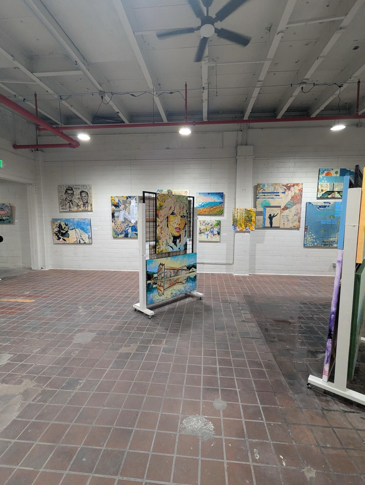 A photo showing the main gallery at Clover24. There are paintings on the wall and art on easels in the middle of the room