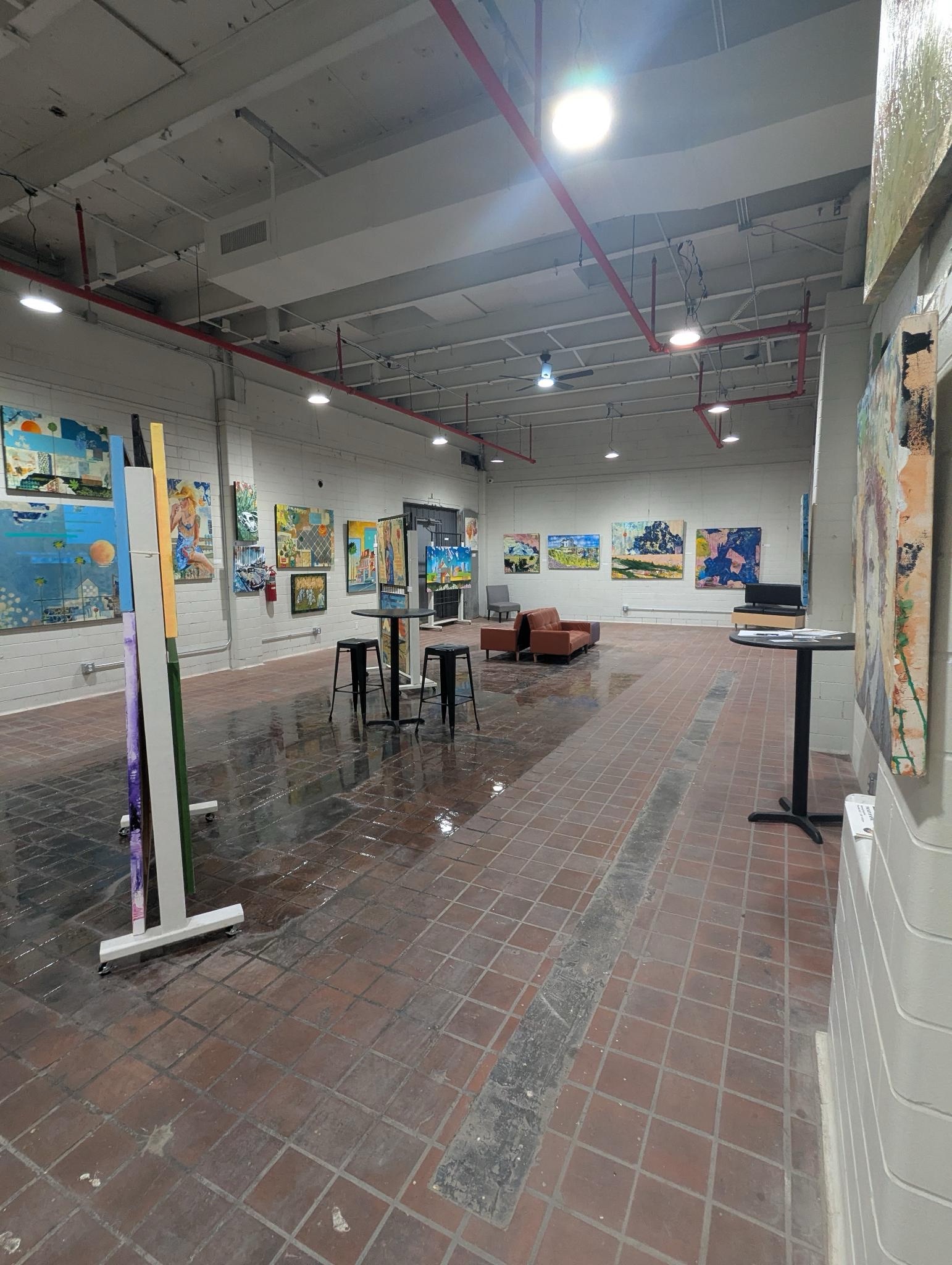 A photo showing the main gallery at Clover24. There are paintings on the wall and art on easels in the middle of the room